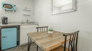 Una cocina compacta con una mesa de madera, dos sillas, un refrigerador azul, un lavamanos y un espejo en la pared.