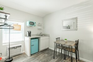 Une cuisine compacte équipée d’un four à micro-ondes, d’un grille-pain et d’un évier. On y trouve une table à manger avec des chaises et une petite plante en pot.