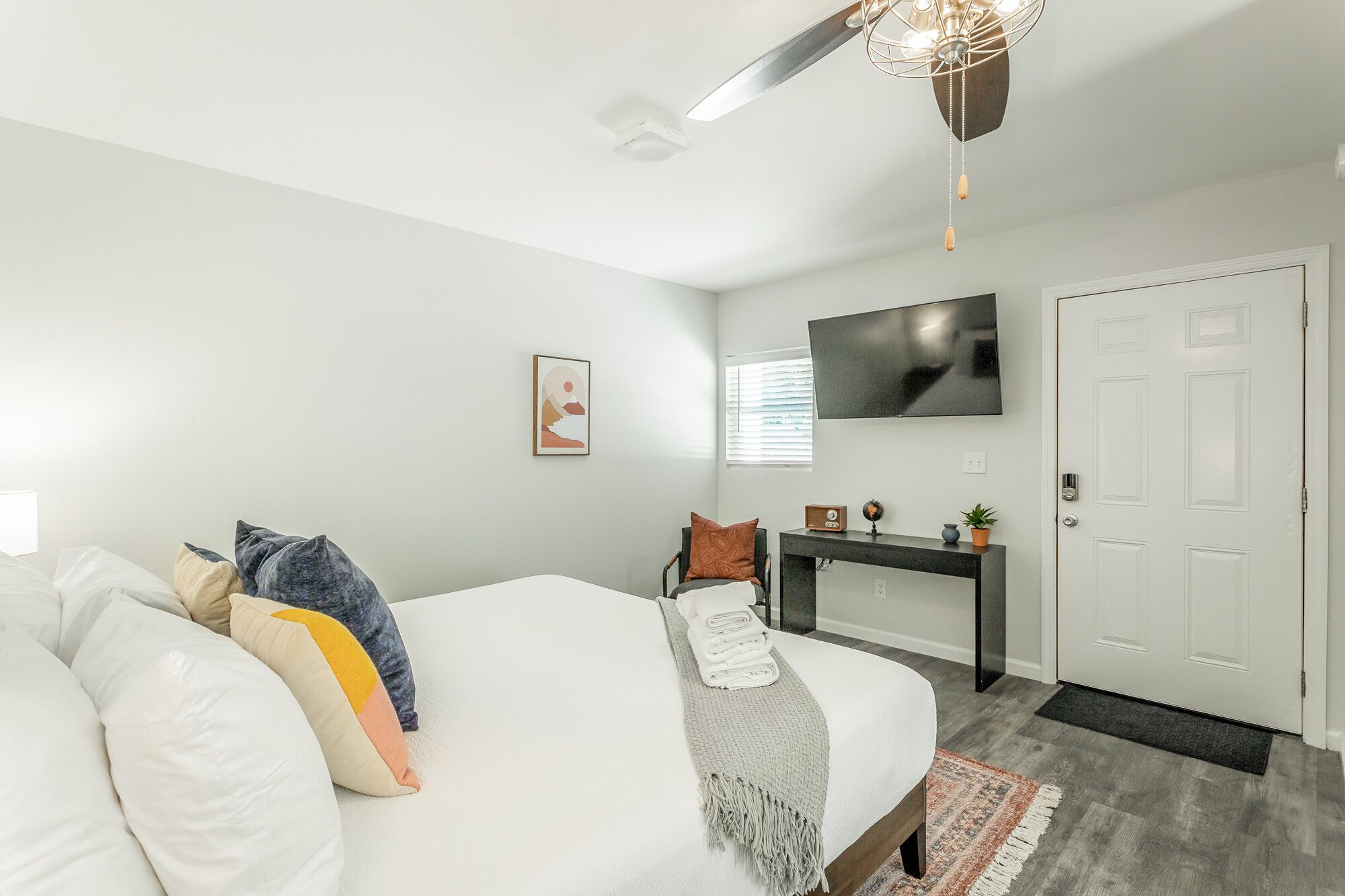 A modern bedroom with a bed, a desk, a TV, and a door.