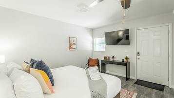 A modern bedroom with a bed, a desk, a TV, and a door.