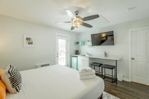 Une chambre moderne équipée d’un lit, d’un ventilateur de plafond, d’un petit coin cuisine et d’un téléviseur fixé au mur.