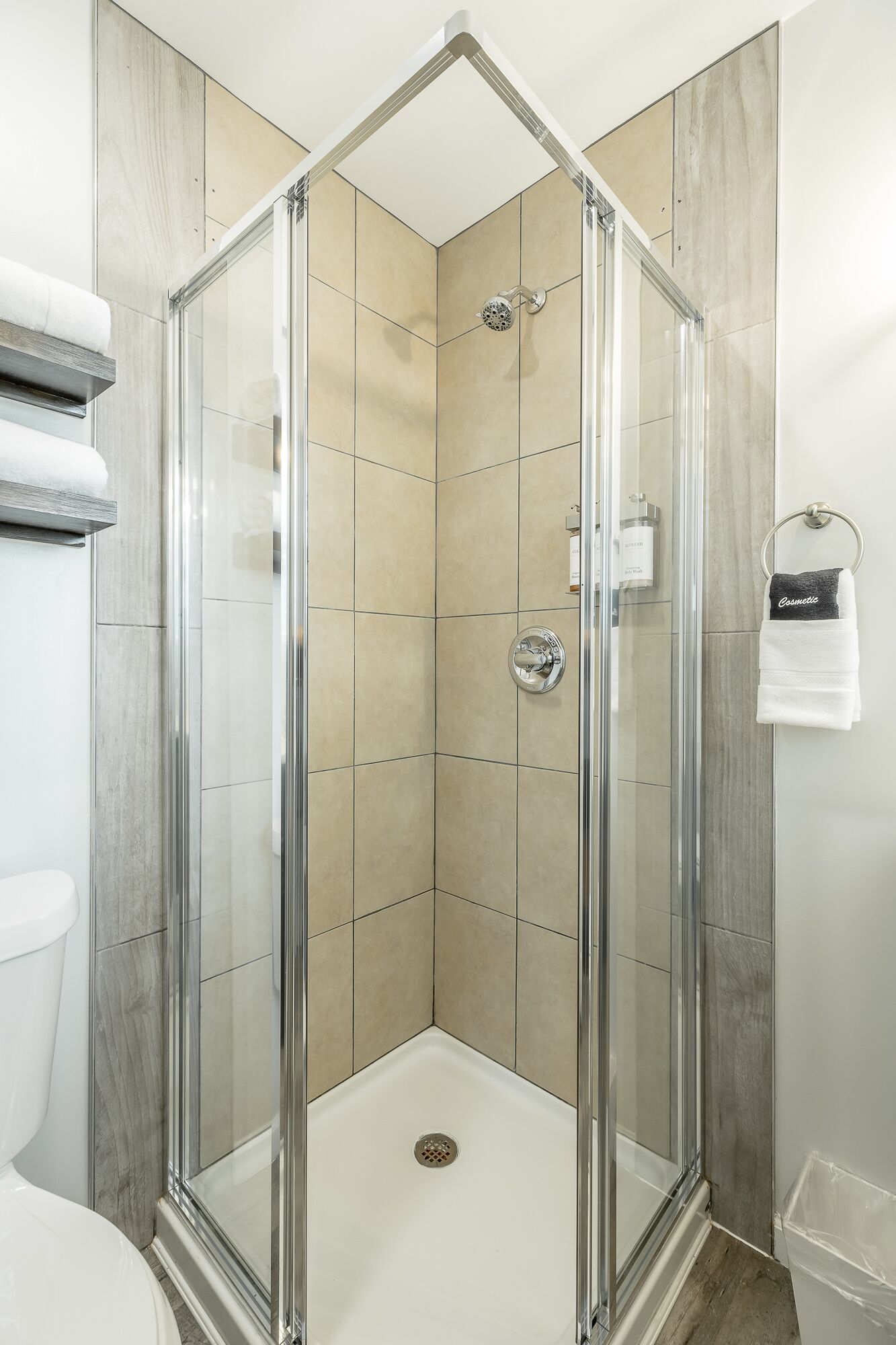 A glass-enclosed shower stall with a white floor, beige tiles, and a glass door.