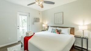 Ein Schlafzimmer mit einem großen Bett, zwei Nachttischen mit Lampen, einem Deckenventilator und einer Tür zum Balkon.