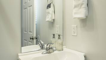 A bathroom with a white sink, two faucets, a mirror with lights, and a towel rack with a white towel and a gray towel.
