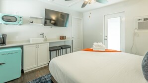 Une chambre d’hôtel moderne équipée d’un lit, d’une kitchenette, d’un ventilateur de plafond, d’une télévision et d’une porte.