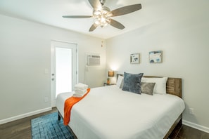 Une chambre à coucher comprenant un lit, un ventilateur de plafond, une table de chevet avec une lampe et deux unités de climatisation fixées au mur.