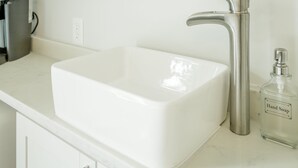 A white rectangular sink with a modern faucet, a clear glass bottle of hand soap, and a white countertop.