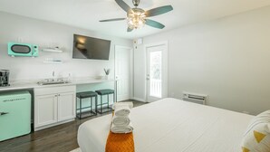 Un dormitorio moderno con cama, ventilador de techo, televisor y kitchenette.