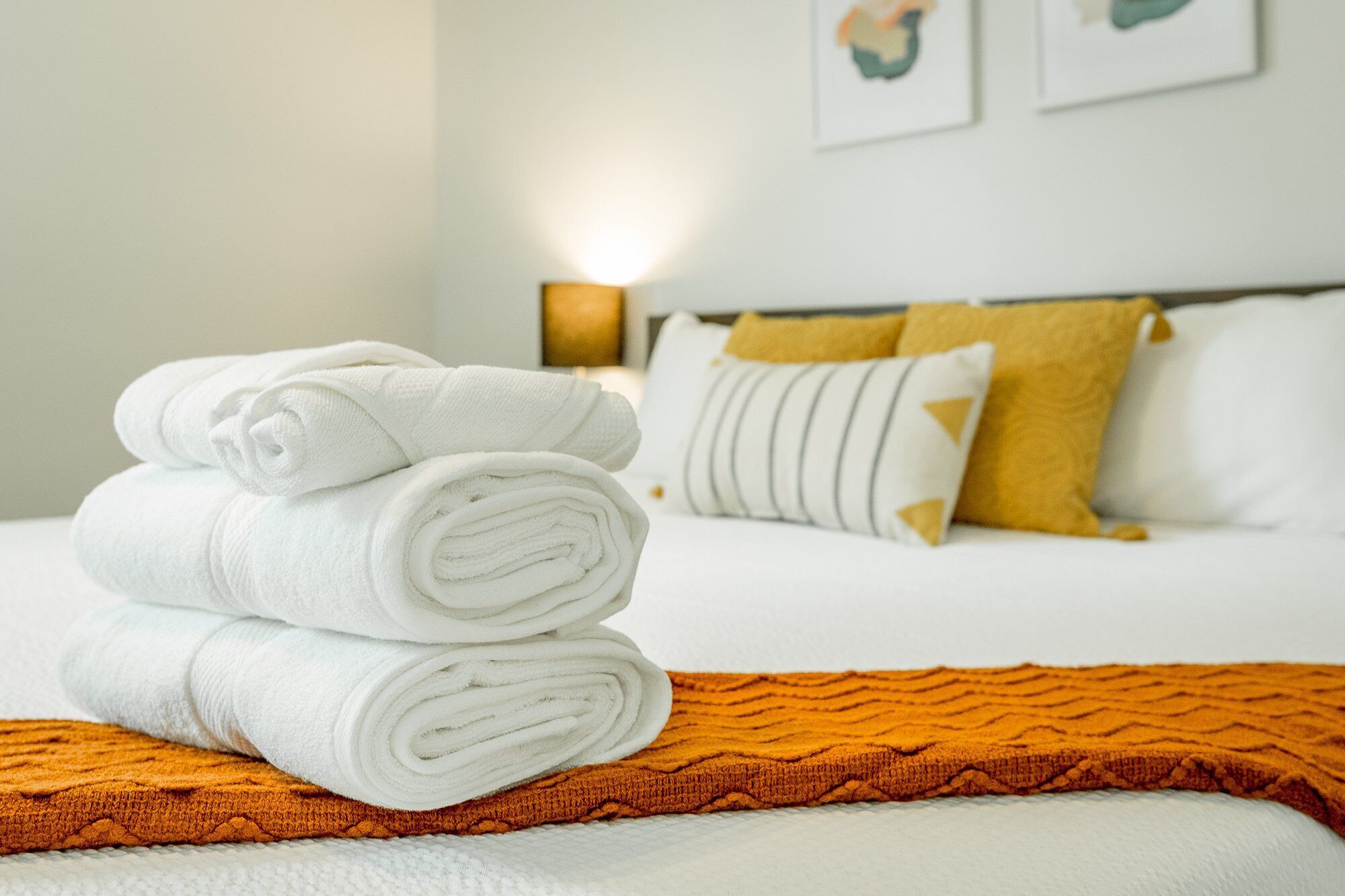 A neatly made bed with white linens and a folded towel on an orange blanket.
