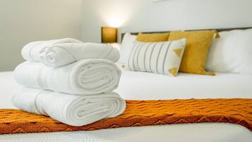 A neatly made bed with white linens and a folded towel on an orange blanket.