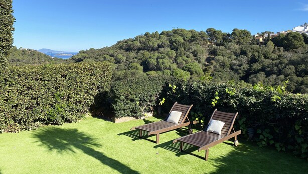 Two wooden lounge chairs with white cushions on a well-manicured lawn, overlooking a lush, green hillside with a clear blue sky above. - House in Begur with swimming pool and castle view - 3 bedrooms, sleeps 5 to 6 (Begur)