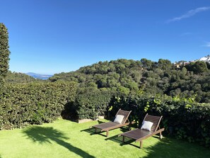 Two wooden lounge chairs with white cushions on a well-manicured lawn, overlooking a lush, green hillside with a clear blue sky above. - House in Begur with swimming pool and castle view - 3 bedrooms, sleeps 5 to 6 (Begur)