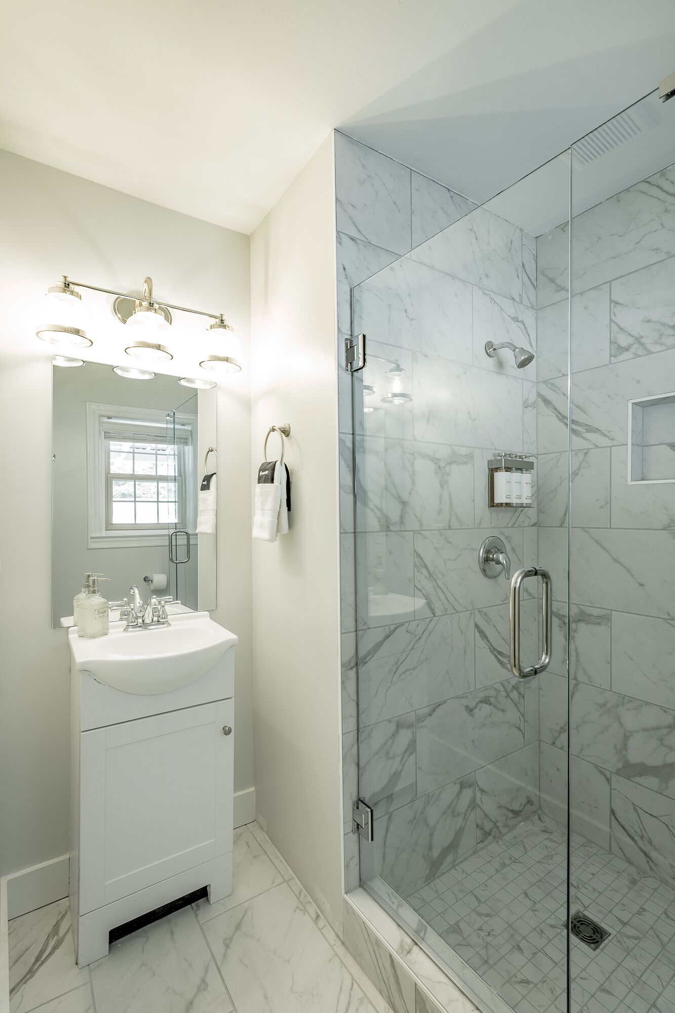 Une salle de bain avec un meuble-lavabo blanc, une cabine de douche en verre et une zone de douche carrelée en marbre.
