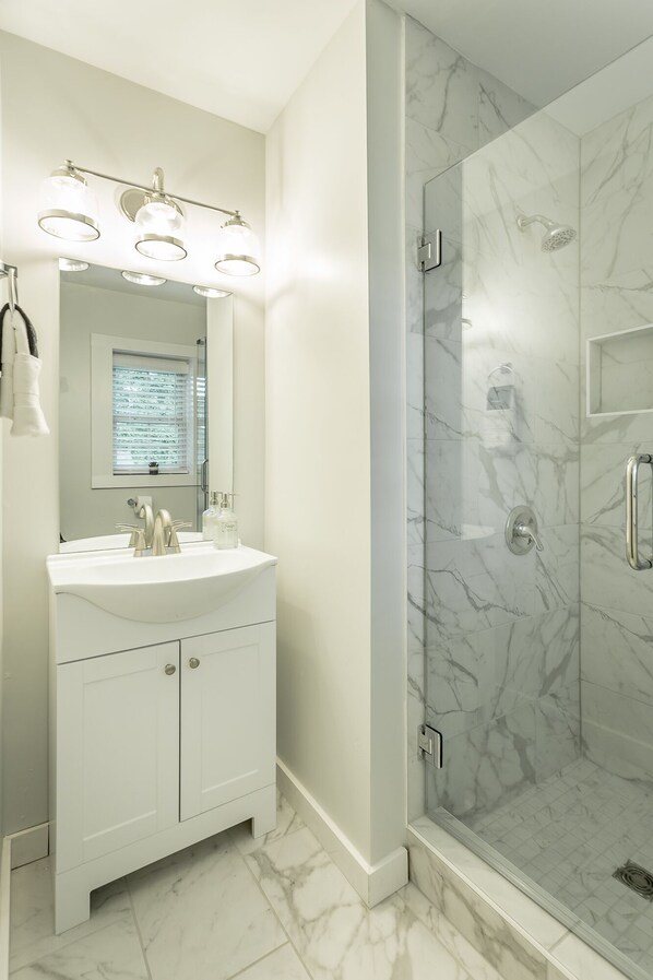Un baño moderno con ducha de mármol y tocador con espejo e iluminación.