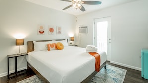 A hotel room with a bed, a ceiling fan, wall art, a door, and a small cabinet. - 10: The Jacobsen Room - A PMI Scenic City Vacation Rental (Chattanooga)
