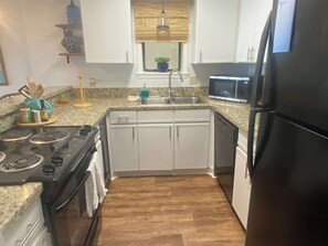 A compact kitchen with a stove, sink, and refrigerator. - Compass Point 506, a beautiful lagoon-front 1BR. Great views, decor & amenities (Gulf Shores)
