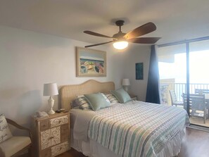 A bedroom with a bed, nightstands, a ceiling fan, a painting, and a view of the ocean.