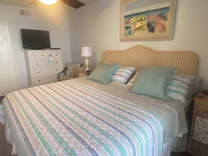 Une chambre à coucher avec un lit, une commode, une lampe, un tableau et un téléviseur.