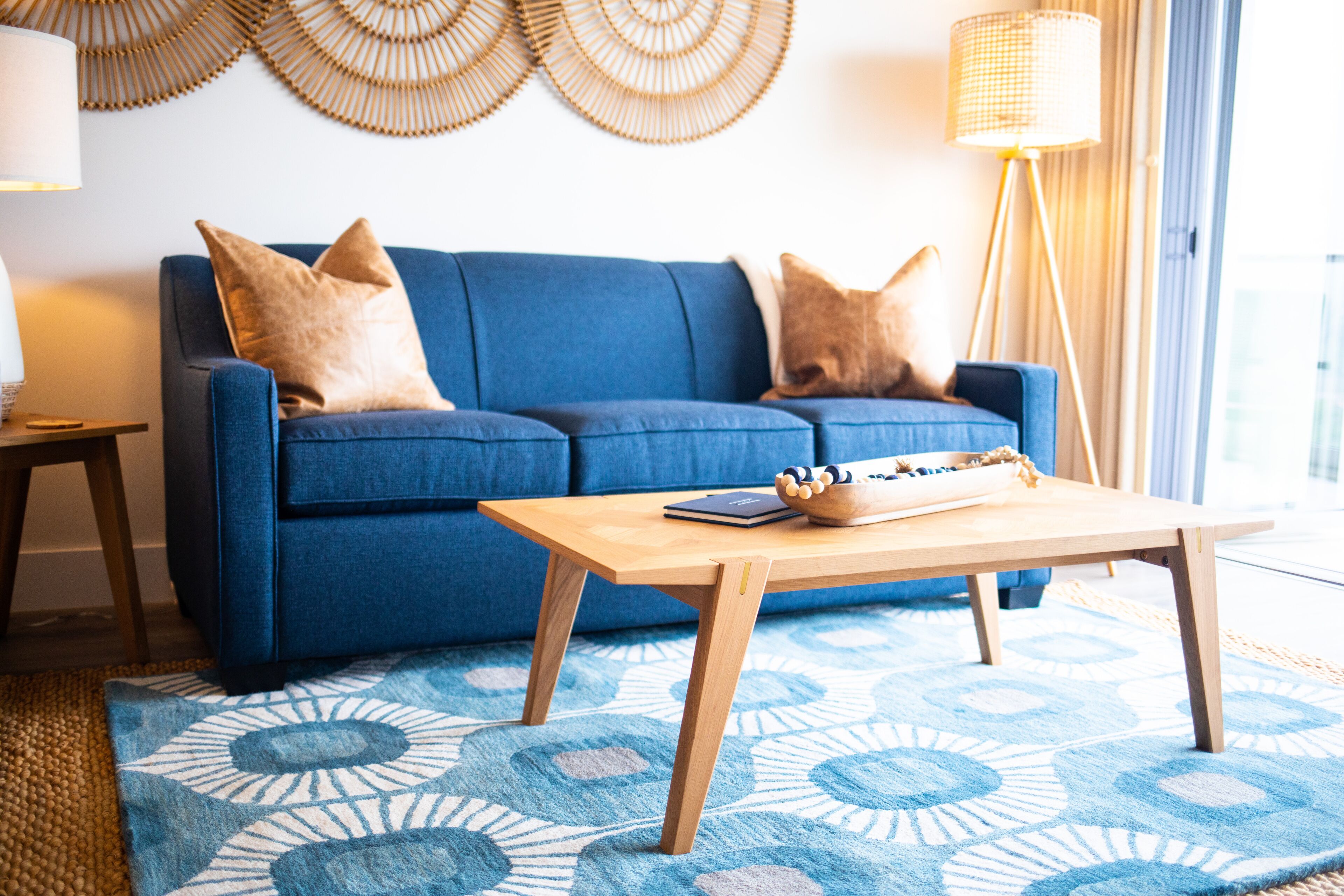 A blue sofa with two pillows, a wooden coffee table, and a patterned rug.