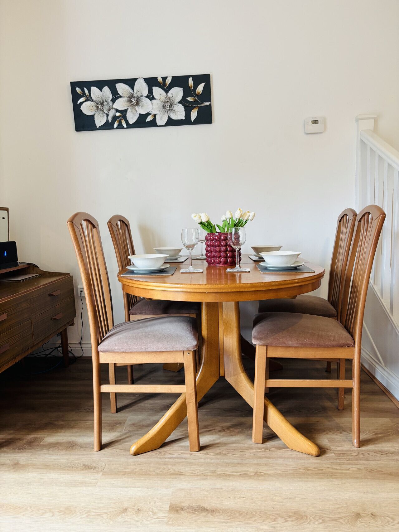 Une table à manger avec quatre chaises, un vase rempli de fleurs et une œuvre d’art florale accrochée au mur.