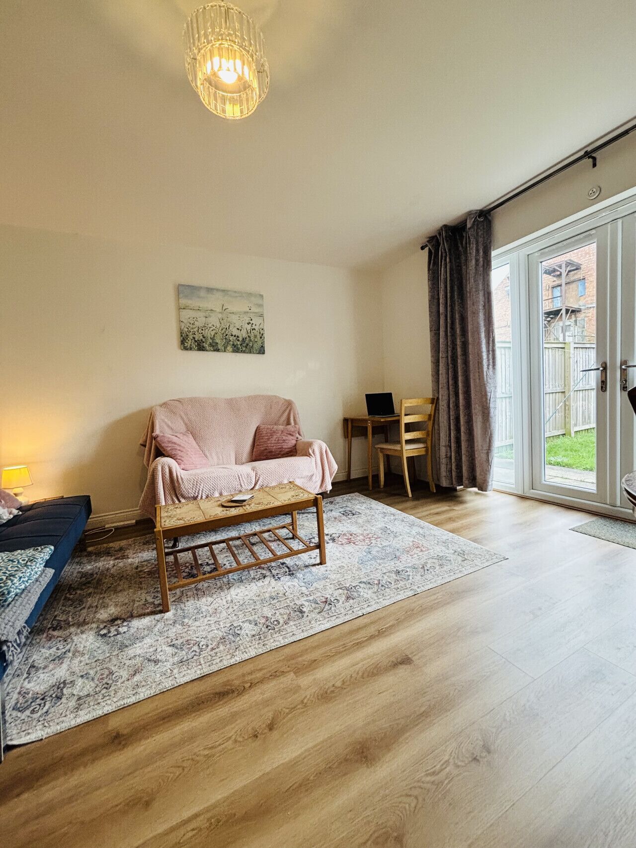 A spacious living room with a sofa, a coffee table, a painting on the wall, and a view through a sliding glass door.