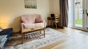 A spacious living room with a sofa, a coffee table, a painting on the wall, and a view through a sliding glass door.