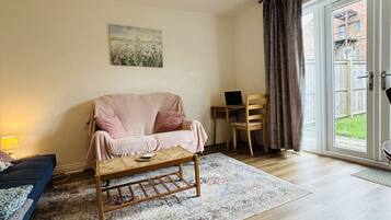A spacious living room with a sofa, a coffee table, a painting on the wall, and a view through a sliding glass door.