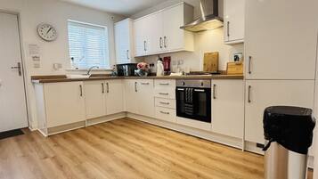 A modern kitchen with white cabinets, a stainless steel range hood, and a black coffee machine.