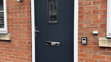 A dark-colored door with a small window and a handle, set in a brick wall with a white trim.
