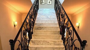 Un escalier en marbre, agrémenté de rampes en fer forgé noir, et bordé de luminaires fixés au mur.