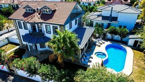Une grande maison avec une piscine, entourée d’arbres et d’autres maisons.