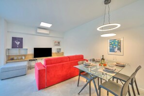 A modern living room with a red sofa, a glass dining table, and a flat-screen TV. - Quadrifoglio, Lugano, Switzerland (Lugano)