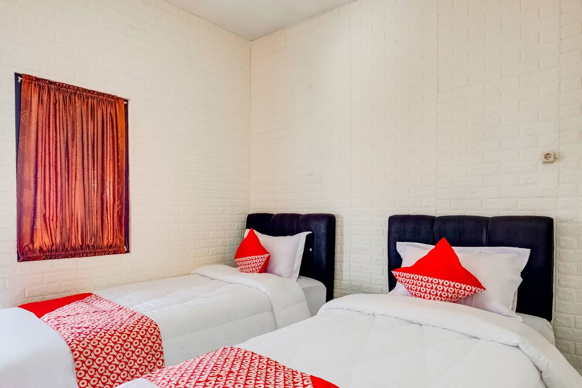 Een hotelkamer met twee bedden, witte bakstenen muren en beddengoed met een rood-wit patroon.