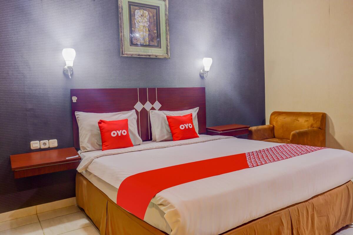 Een hotelkamer met een bed, twee nachtkastjes, een stoel en een aan de muur hangend schilderij.