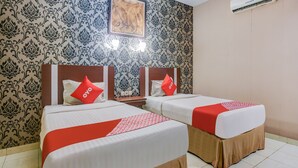 A hotel room with two beds, each with a red and white bedspread, and a patterned wallpaper. - OYO 3936 Hotel Trisula Makassar (Makassar)