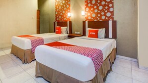 A hotel room with two beds, each with a red and white patterned bedspread, a wooden headboard, and a mirror above the beds. - OYO 3936 Hotel Trisula Makassar (Makassar)