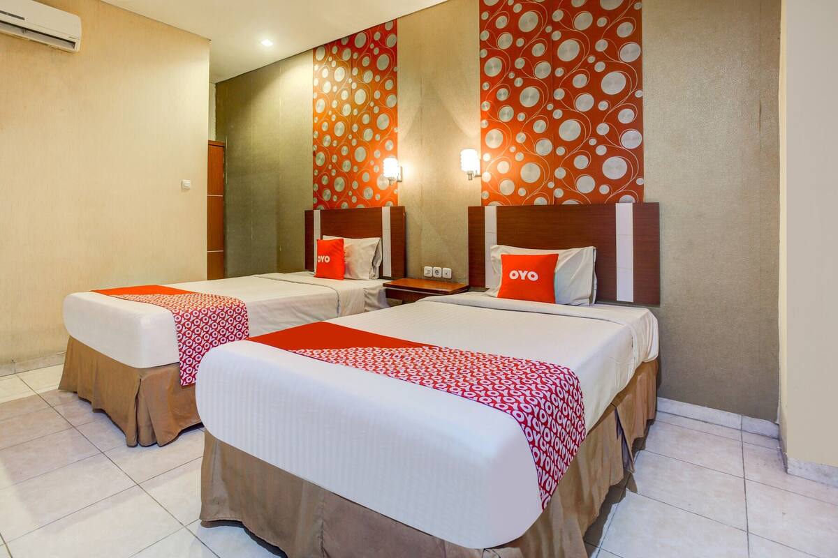 Een hotelkamer met twee bedden, elk met een rood-wit beddeken, een houten hoofdbord en een spiegel boven de bedden.