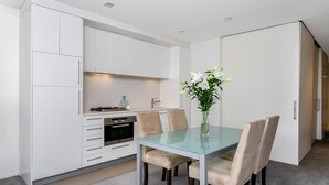 A modern kitchen with white cabinets, a glass dining table, and beige chairs.