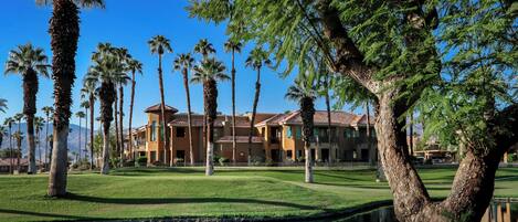 A resort with palm trees, a pond, and a building with a tiled roof.