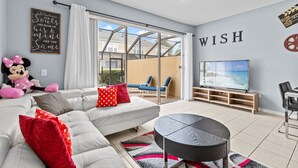 A modern living room with a white sofa, red and white pillows, a black coffee table, a television, and a large window with a view of the outside. - The Wish House, just miles from Disney World (Four Corners)
