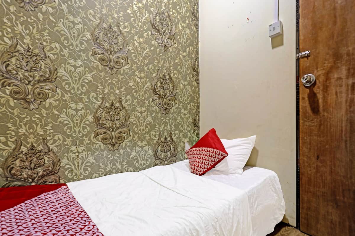 A single bed with white bedding and a red pillow, a wooden door, and patterned wallpaper.