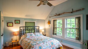 A bedroom with a bed, a ceiling fan, a window with curtains, and a wall-mounted lamp. - Cottage in Downtown Mystic (Mystic)