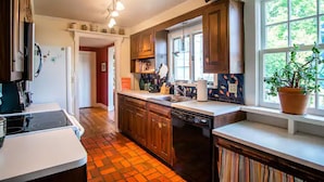 A kitchen with wooden cabinets, a dishwasher, a stove, and a window with a plant. - Cottage in Downtown Mystic (Mystic)