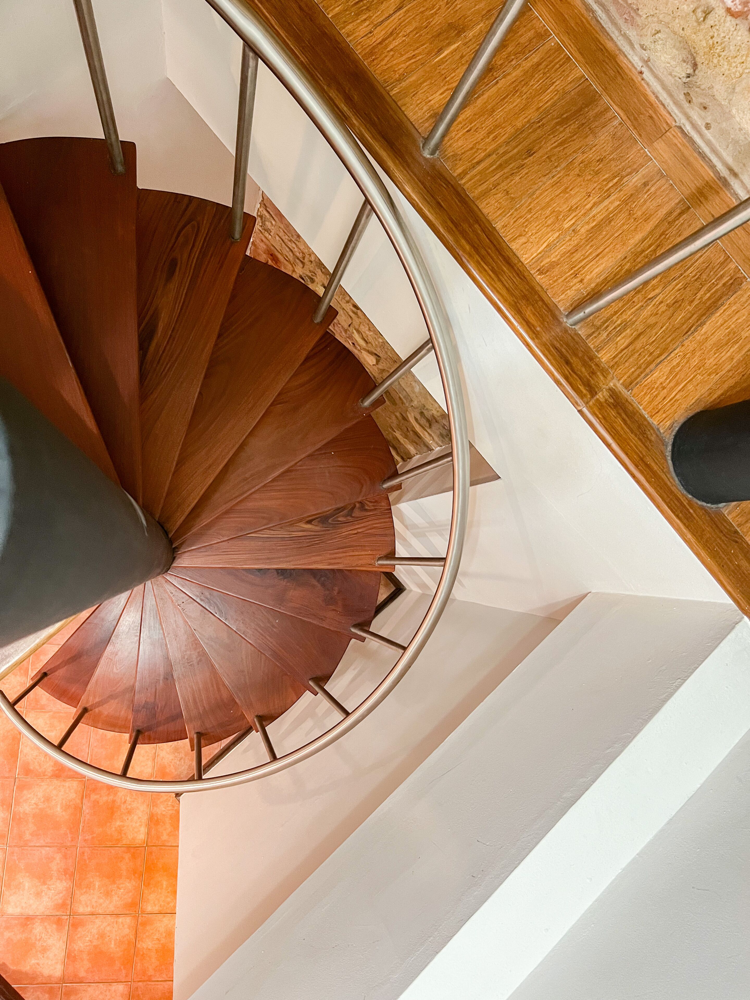 A spiral staircase with wooden steps and metal handrails, leading to a landing with a wooden floor and white walls.