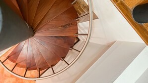 A spiral staircase with wooden steps and metal handrails, leading to a landing with a wooden floor and white walls.