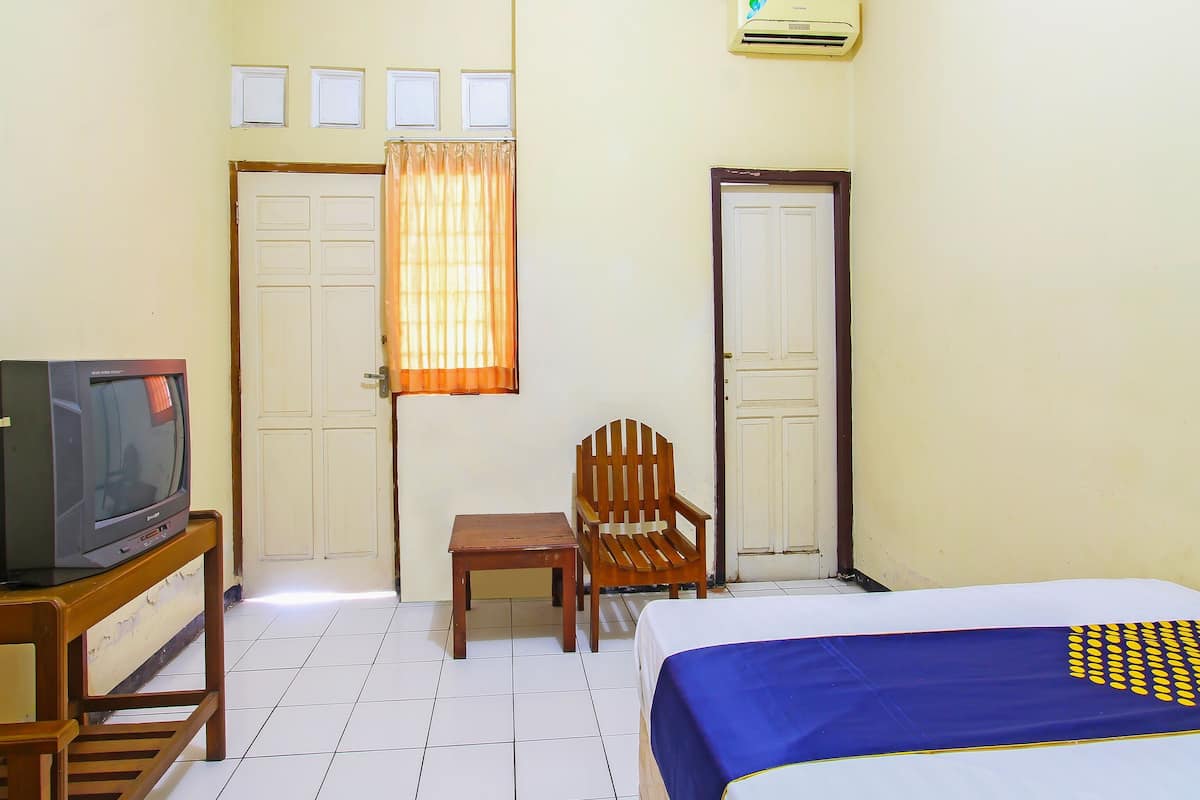 Une chambre d’hôtel avec un lit, un téléviseur posé sur un meuble en bois, une chaise, une petite table et une fenêtre avec des rideaux.