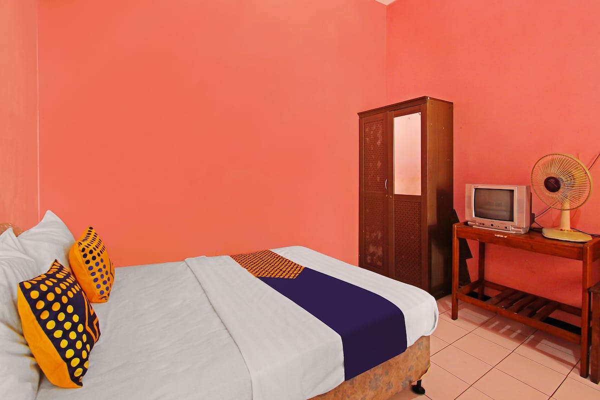Une chambre à coucher avec un lit, des oreillers, une armoire, une télévision et un ventilateur.