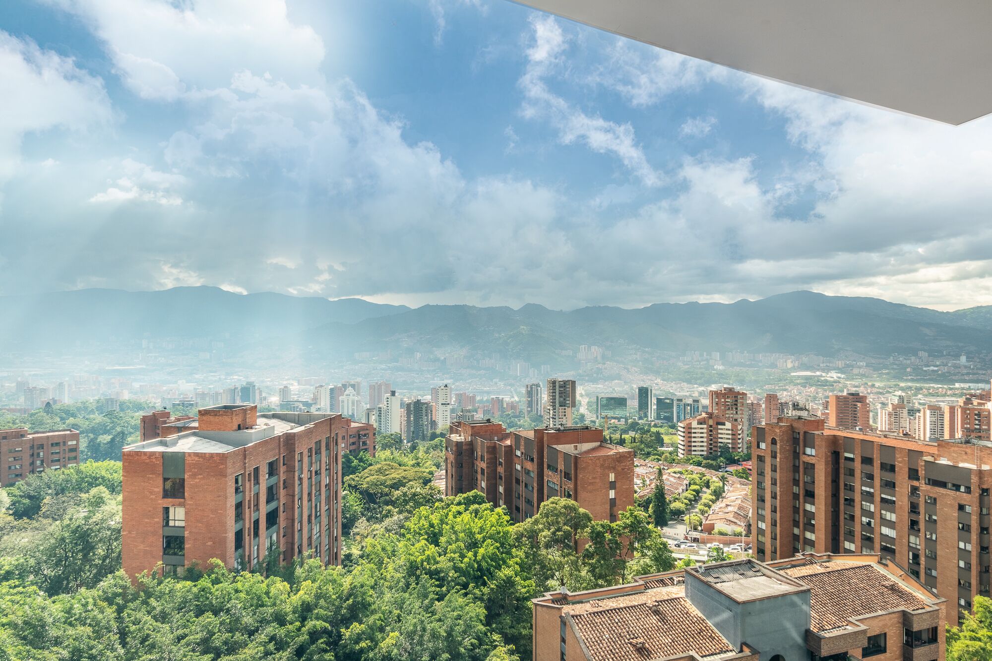 Un ensemble immobilier résidentiel composé de plusieurs immeubles à étages, entouré d’arbres verdoyants et adossé à un paysage montagneux.
