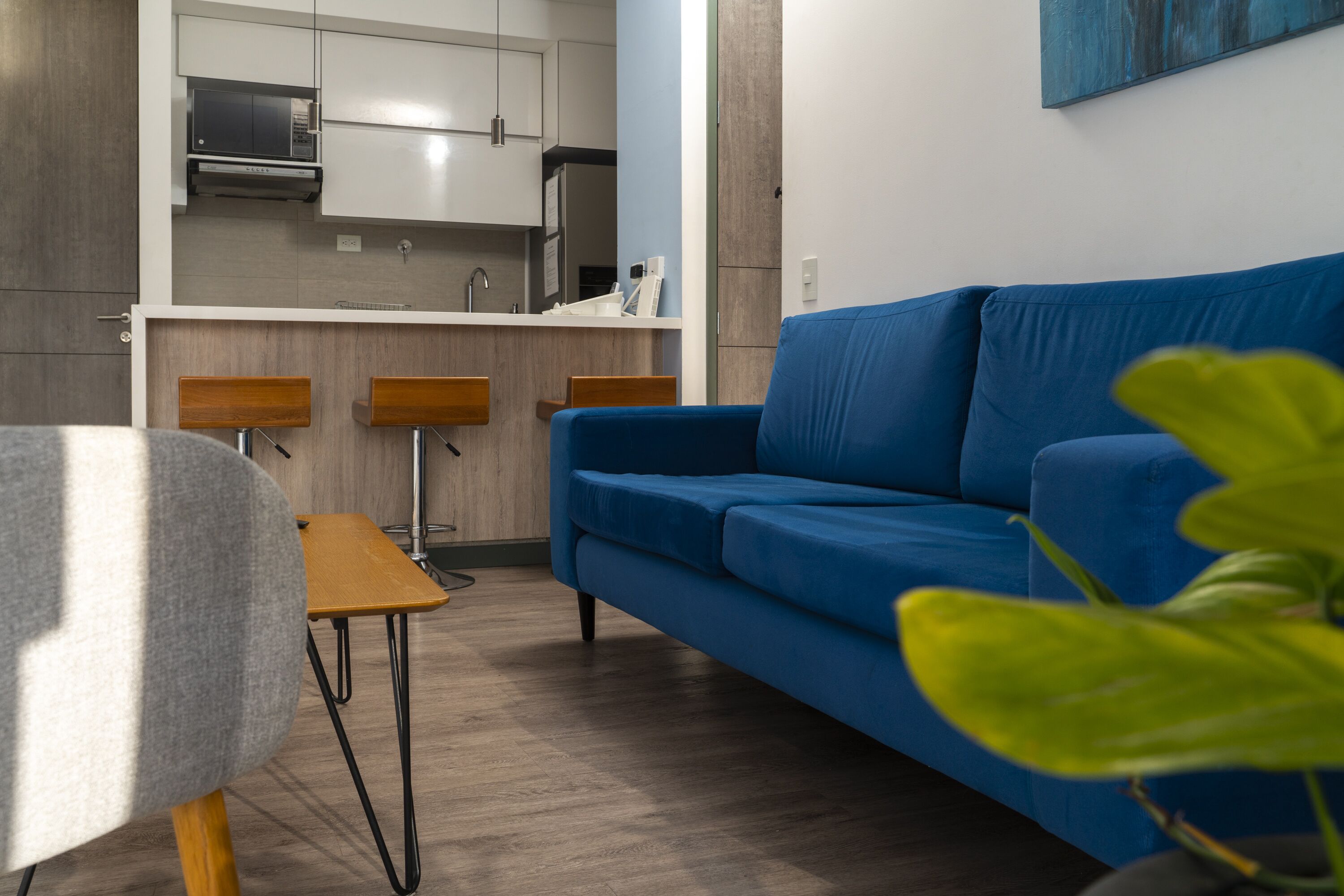 Een moderne woonkamer met een blauwe bank, een houten eettafel en een keuken op de achtergrond.