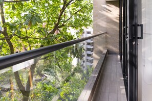 Un balcon doté d’une balustrade en verre, offrant une vue sur un arbre et des immeubles.
